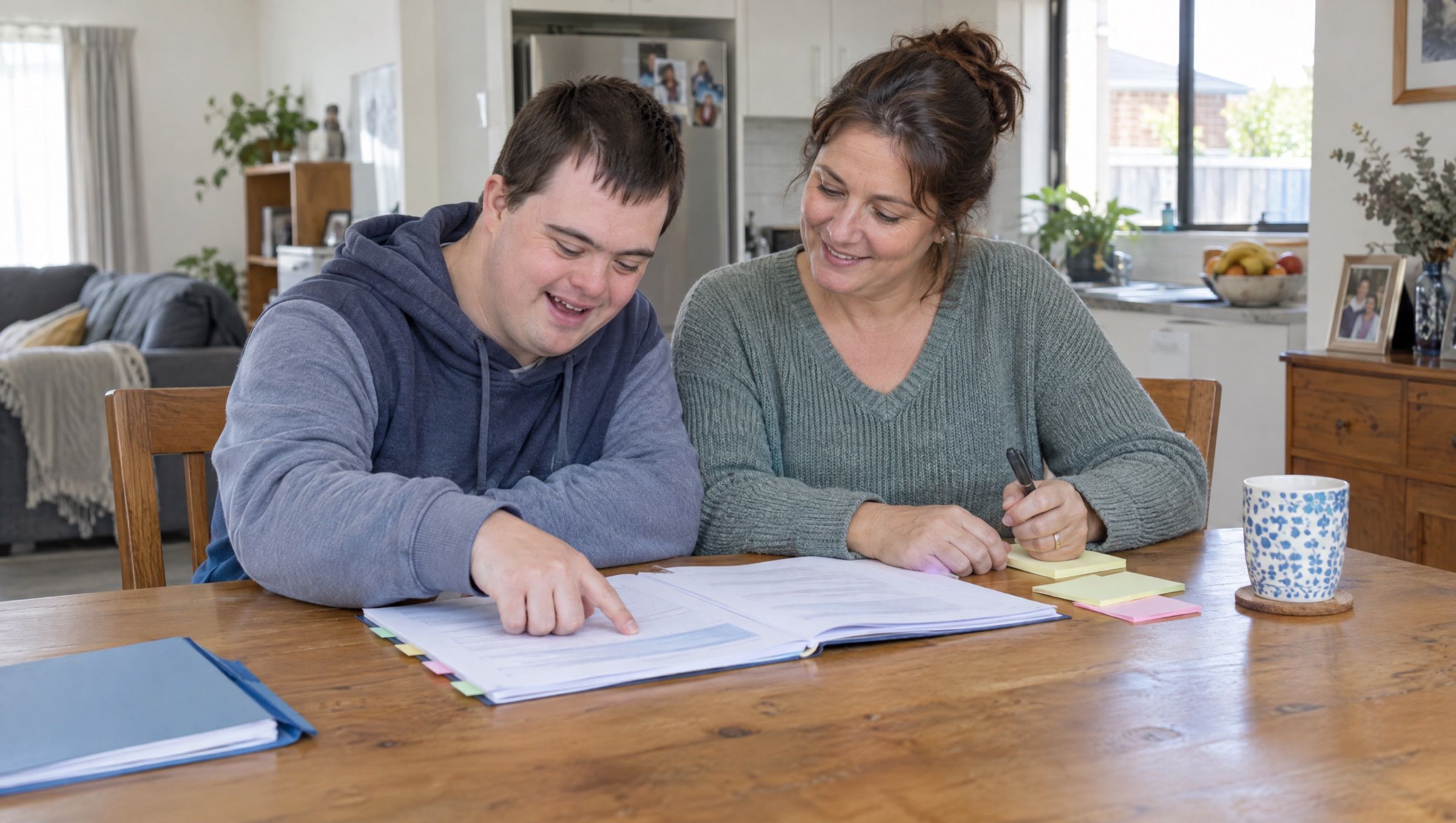 A young man and his mother reading through a printed NDIS plan together at the kitchen table.